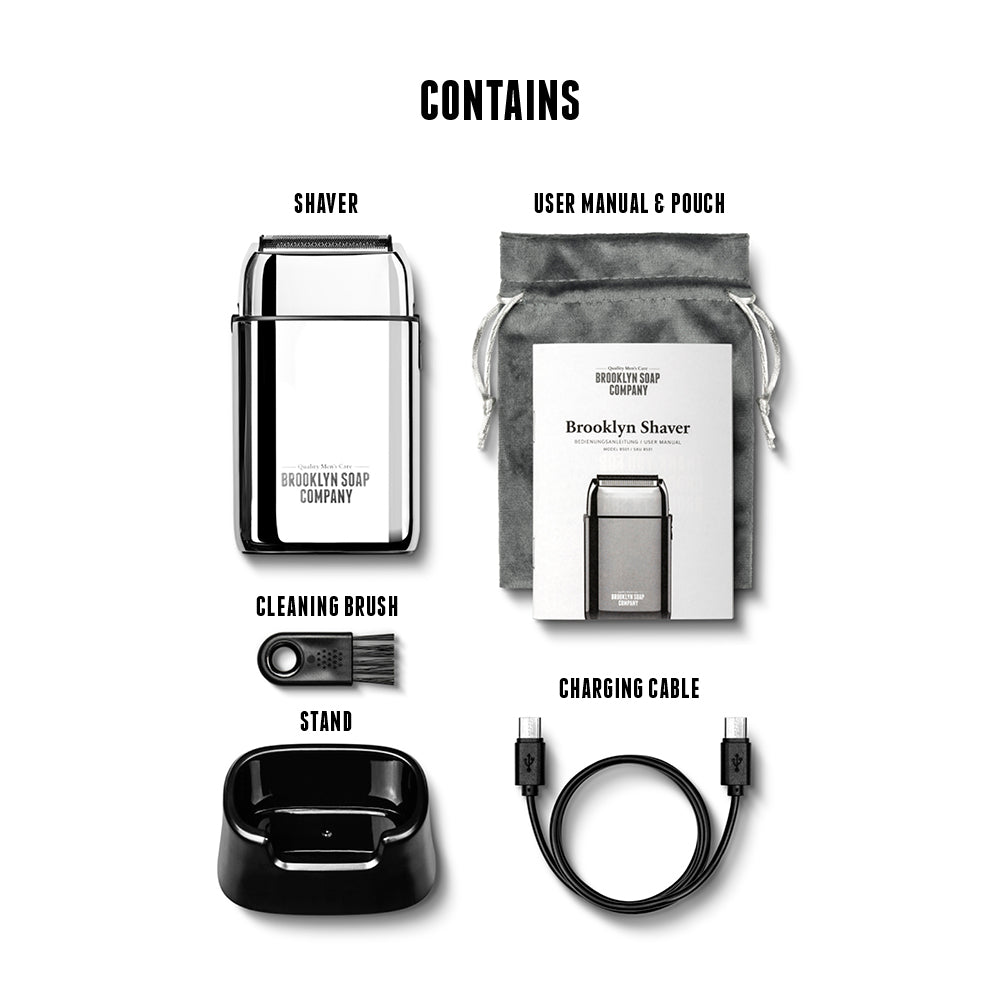 Flat lay of the Brooklyn Soap Company Shaver package contents: electric shaver, user manual with grey drawstring pouch, black cleaning brush, black stand, and USB-C charging cable, all labeled clearly.[INT][EU]